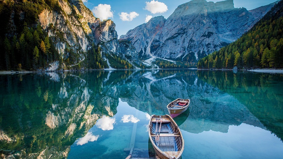 clear blue water, huge mountains and green trees, two wooden boats in the middle of the water