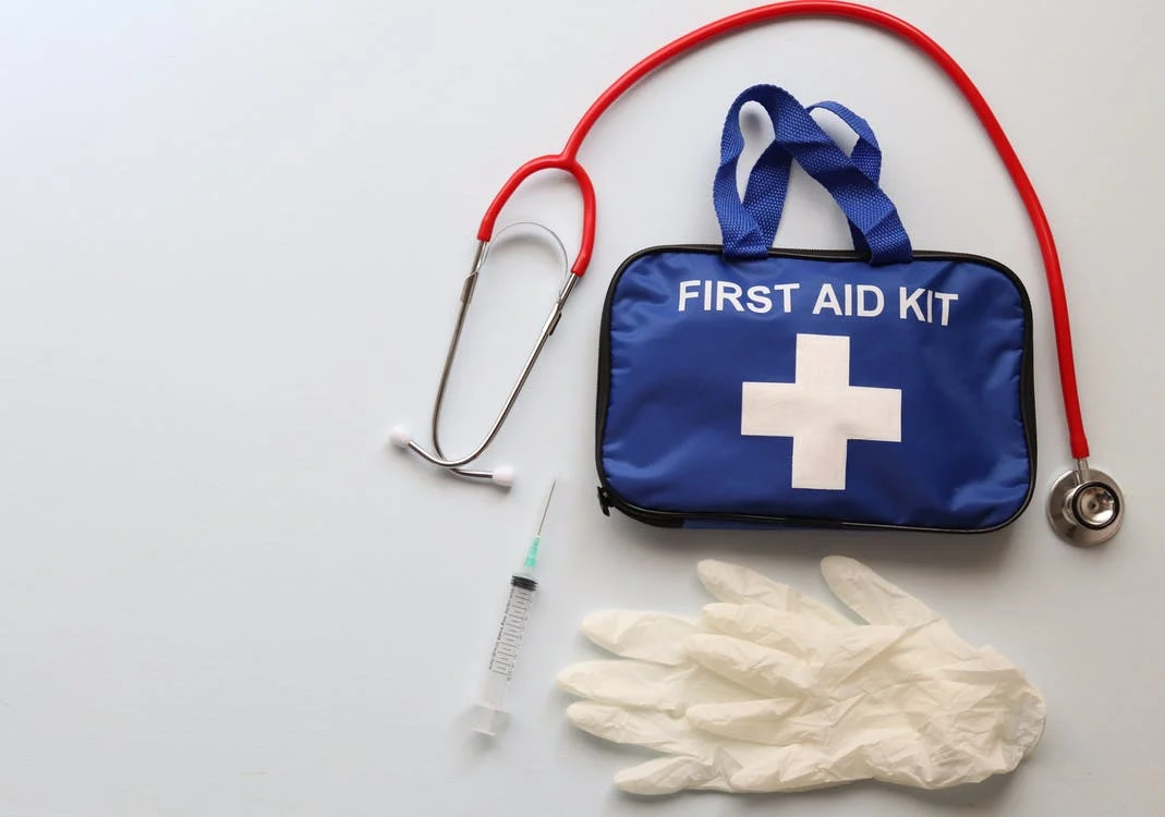 a flatlay of a blue first aid kit, a stethoscope, a syringe, and a pair of gloves