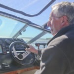 a senior man steering a yacht on a sunny day while looking at the GPS