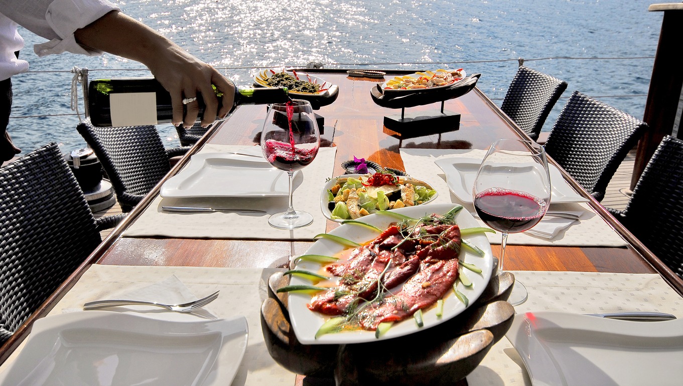 a-table-setting-with-meals-on-the-boat-and-a-server-pouring-wine