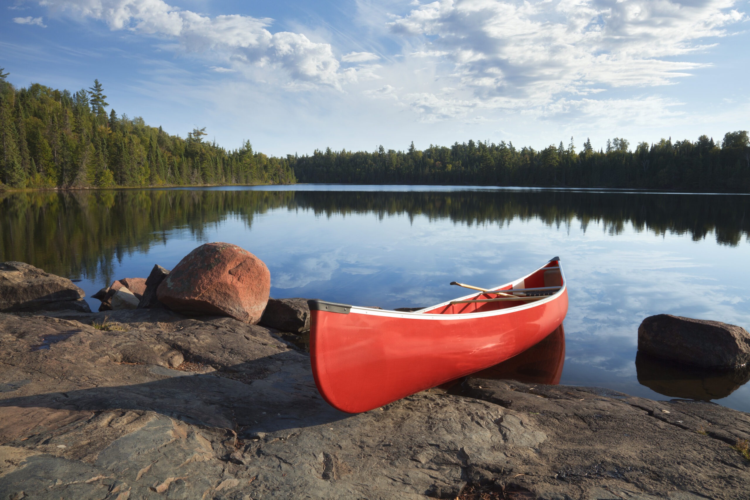 red-canoe-on-rocky-shore-of-calm-northern-lake