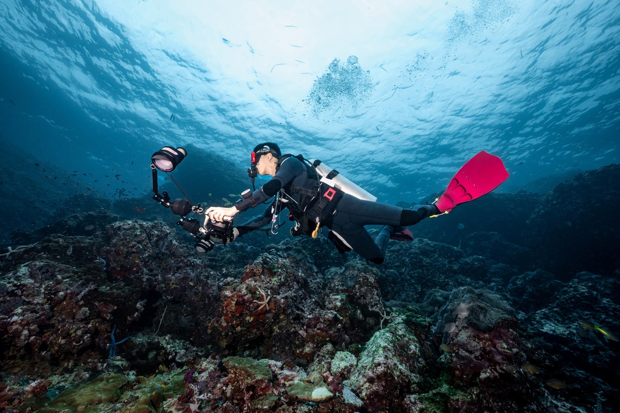 scuba-diver-with-camera-diving-over-coral-reef-in-thailand